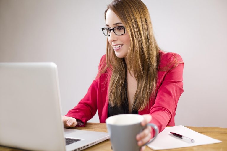 smiling female accountant working at her laptop with her mug, paper and a pen