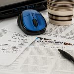 A tabletop covered in tax paperwork a mouse, a coffee cup and a pen