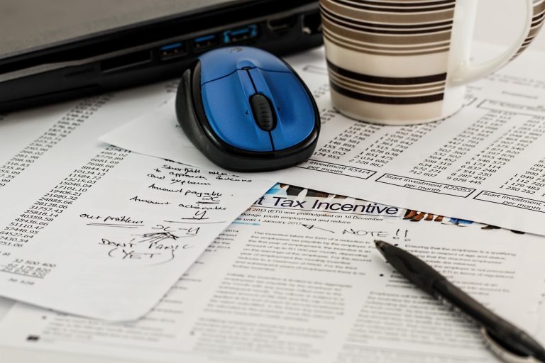 A tabletop covered in tax paperwork a mouse, a coffee cup and a pen